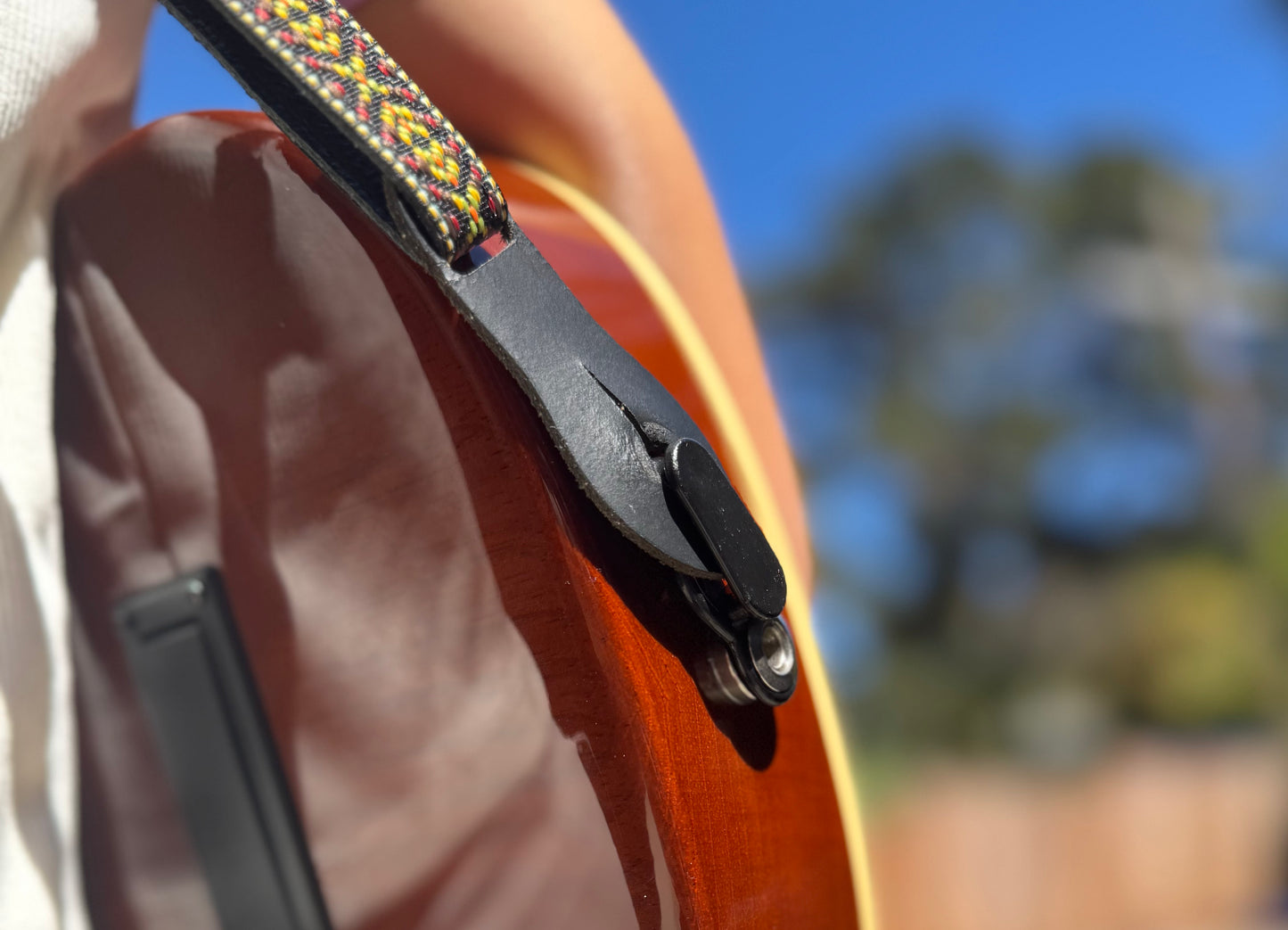 Close-up of a person holding an acoustic electric ukulele with a strap lock.