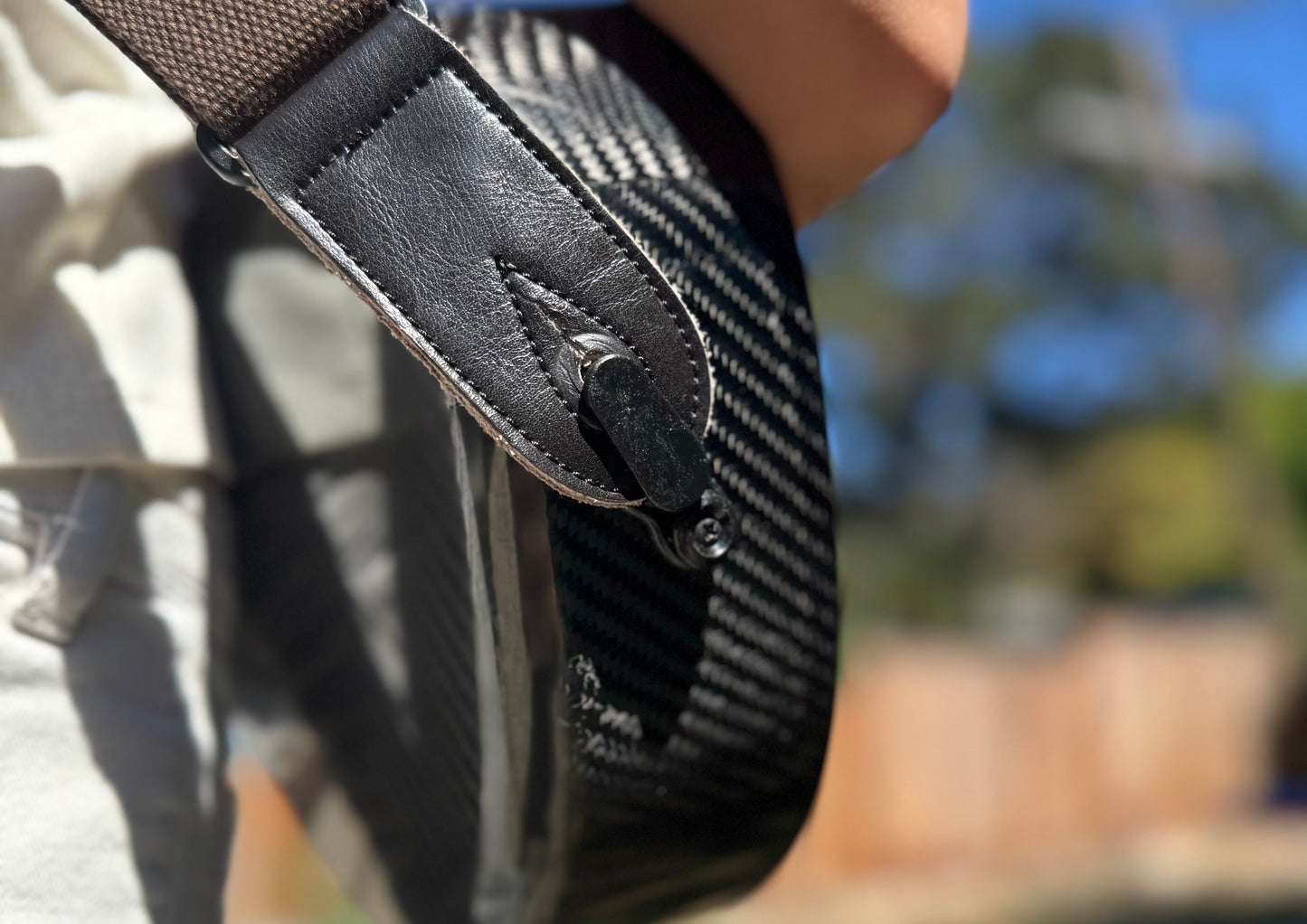 Close-up of a person holding a carbon fiber ukulele with a strap lock fastened to a standard end pin.